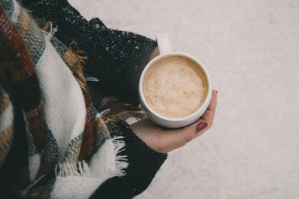 Warm cup of coffee in hands wrapped in a plaid scarf, perfect for a winter chill.